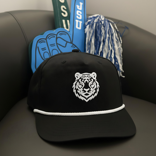 Black cap with white tiger logo on a couch with blue and white pom-poms and green and white letters in the background.